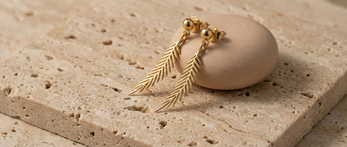 Solid gold feather drop earrings by Larisa Beaumont on travertine stone, British jewellery